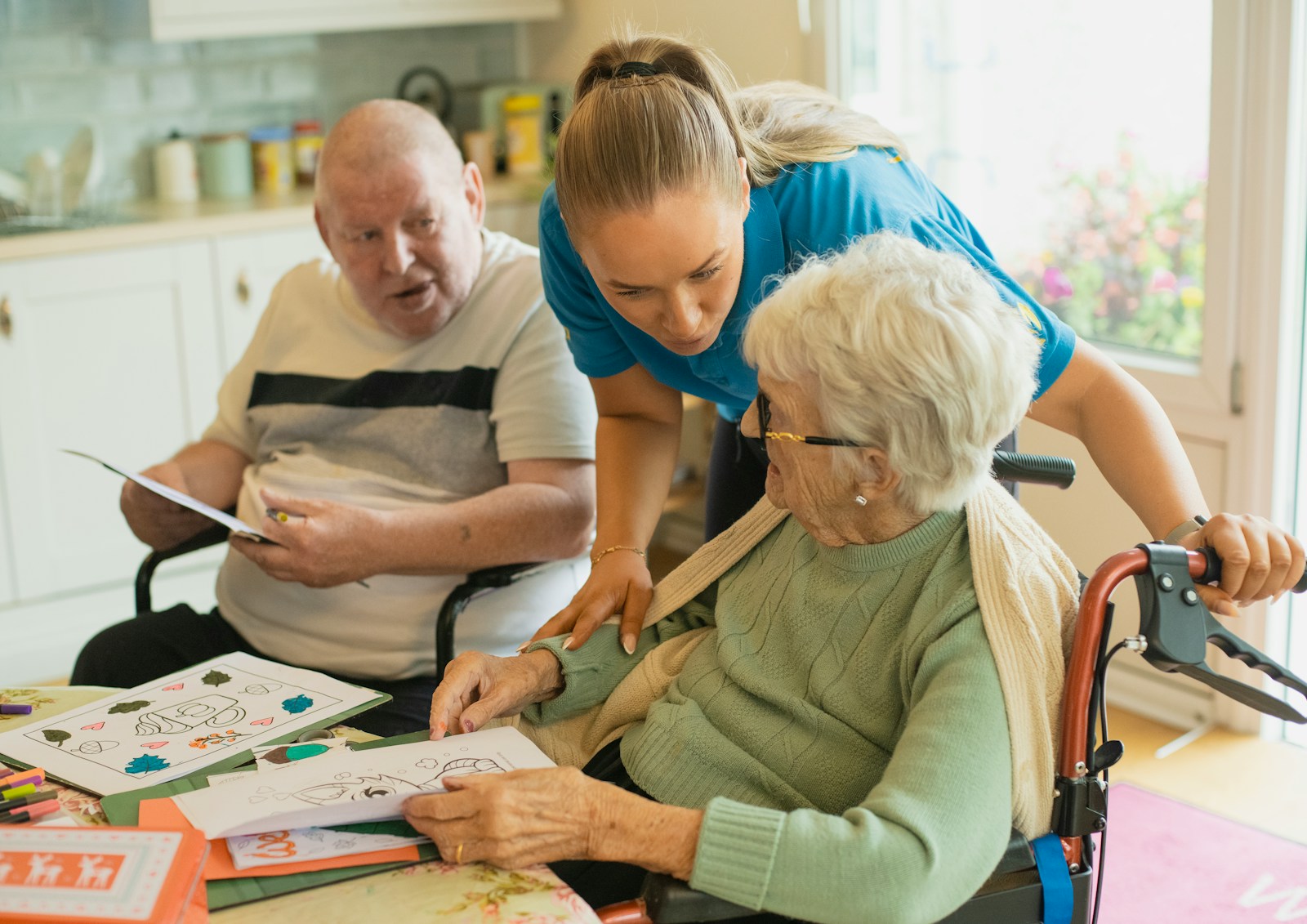 A care worker supporting two older adults with an activity