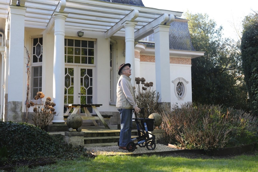 An older adult using a walking aid outside a home
